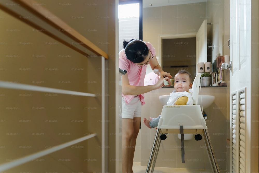アジアの小さな幼児の男の子は、自宅のバスルームで電気かみそりで母親に散髪されます。
