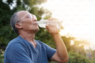 Hombre mayor asiático bebiendo agua después del ejercicio en el fondo al aire libre del parque.