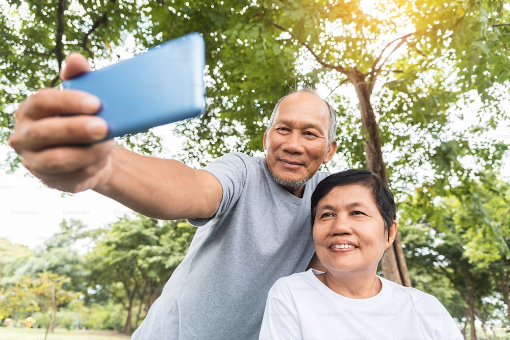 Couple de personnes âgées asiatiques prenant des photos selfie avec un smartphone au parc en plein air. Visage souriant.