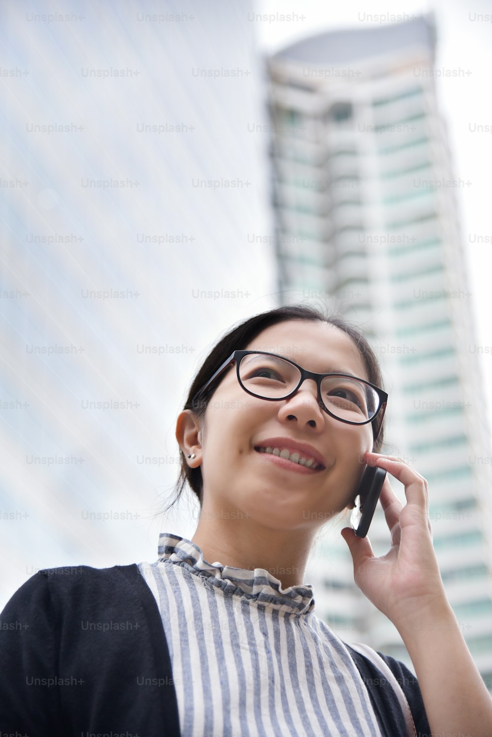 아시아 비즈니스 우먼은 도시의 고층 빌딩 배경에서 휴대폰으로 사업을 이야기합니다.
