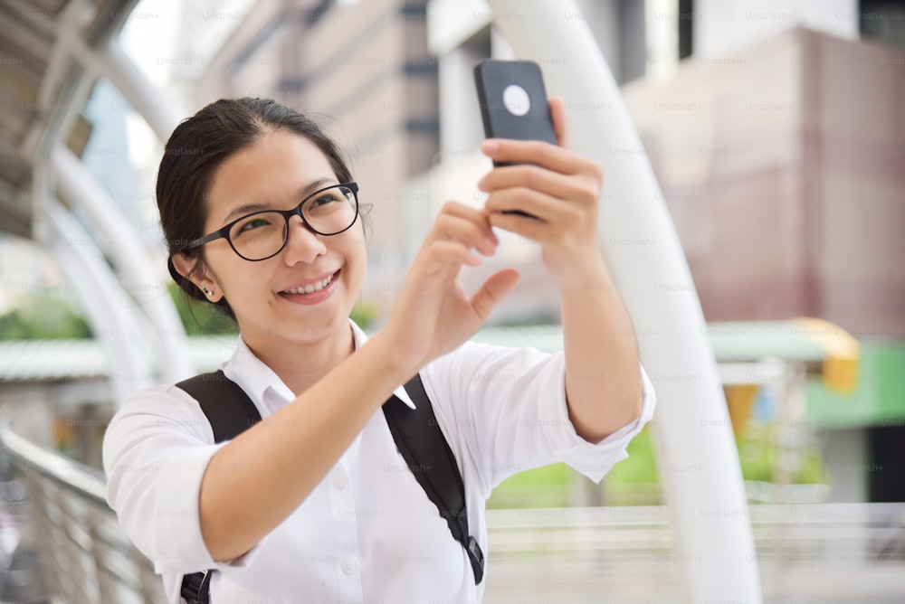 Mulher chinesa usa óculos em camisa branca tirando foto com seu smartphone. Espaço de cópia.