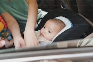 Madre asiática ayudando a su pequeño hijo a abrocharse el cinturón en su asiento de seguridad en el automóvil