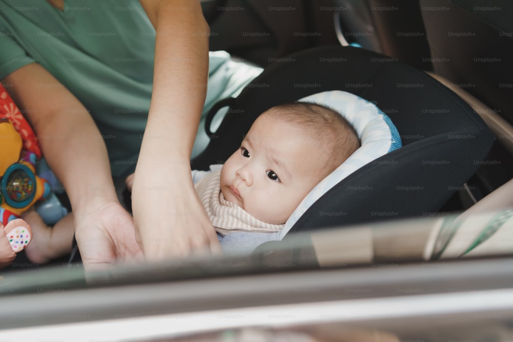 Asian Mother helping her little baby boy son to fasten belt on his car seat in car