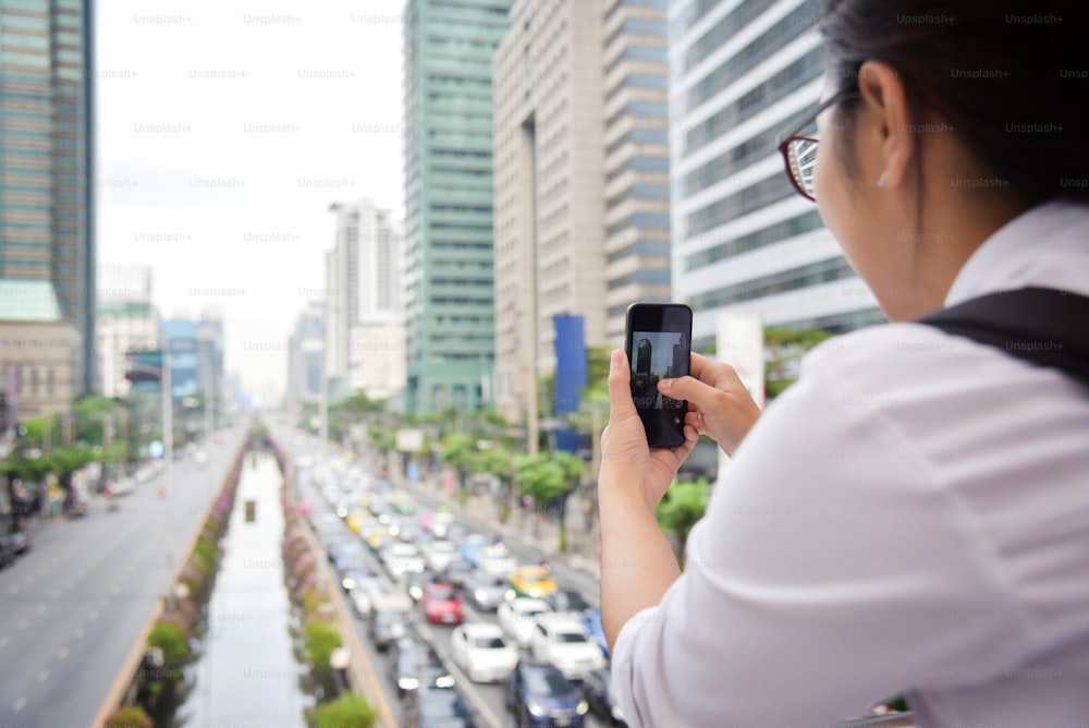 Chinese Woman taking photo with her smart phone on the traffic jam and buildings background in the city. Copy space.