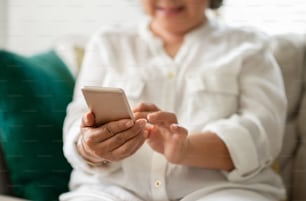 Mujer mayor asiática feliz usando un teléfono inteligente en su casa. Divirtiendo.