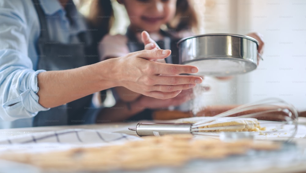 Mom and daughter having fun during sprinkling flour over dough in the kitchen.