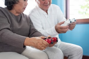 손에 집중하십시오. 아시아 노부부는 조이스틱을 들고 함께 비디오 게임을 한다.