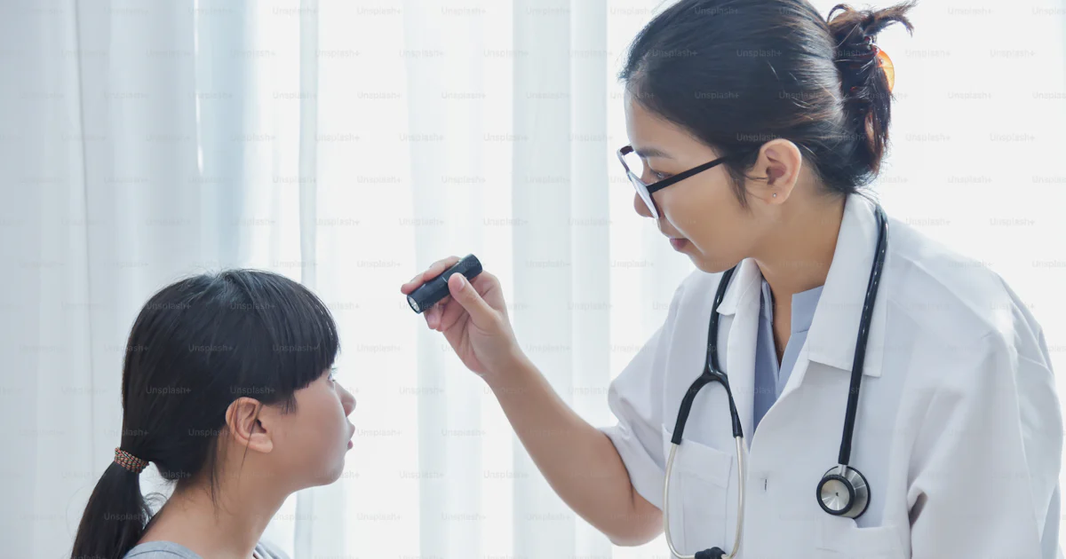 若いアジアの女性医師は、診療所で懐中電灯で小さな女の子の患者の目をチェックする眼鏡をかけています。の写真 – 医者 Unsplashの写真