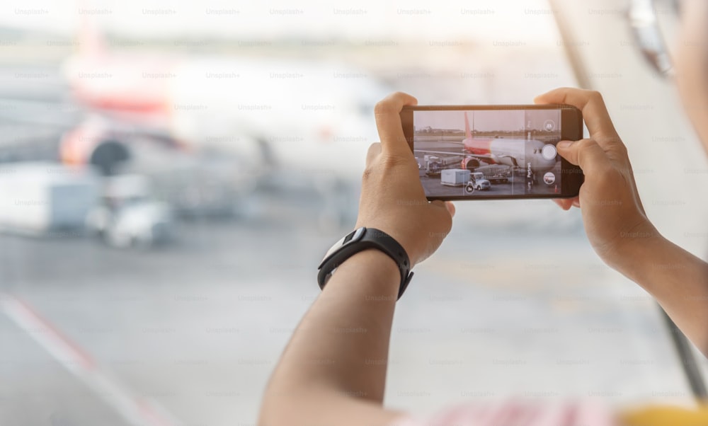 Una viajera asiática disfruta tomando fotos de avión con su teléfono inteligente en el aeropuerto.