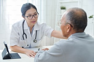 Young Asian Female doctor comforting senior male patient in medical office.