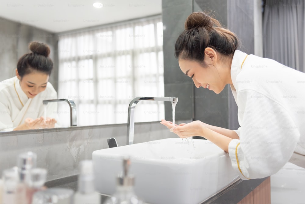 Portrait of beautiful Asian girl is washing her face at basin in her home bathroom.