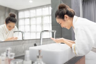 Ritratto di bella ragazza asiatica si sta lavando il viso al lavandino nel suo bagno di casa.