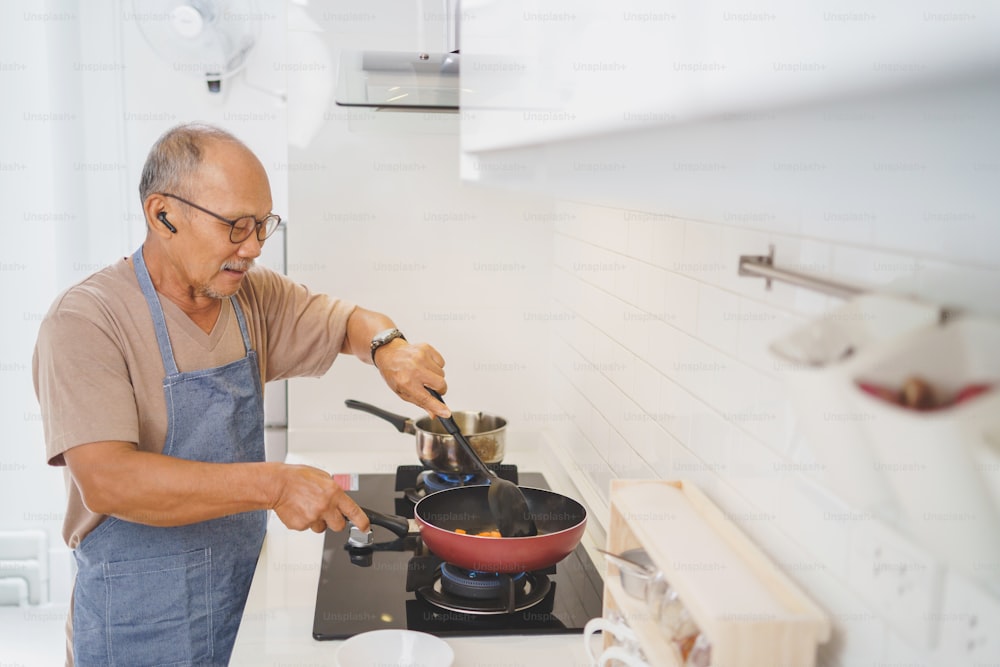 Glücklicher asiatischer reifer erwachsener Mann mit Brille Kochen in der Küche, Essen zubereiten.