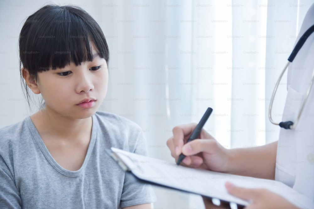 Doctora asiática tomando nota en papel de lista de verificación para una niña pequeña pacientes.
