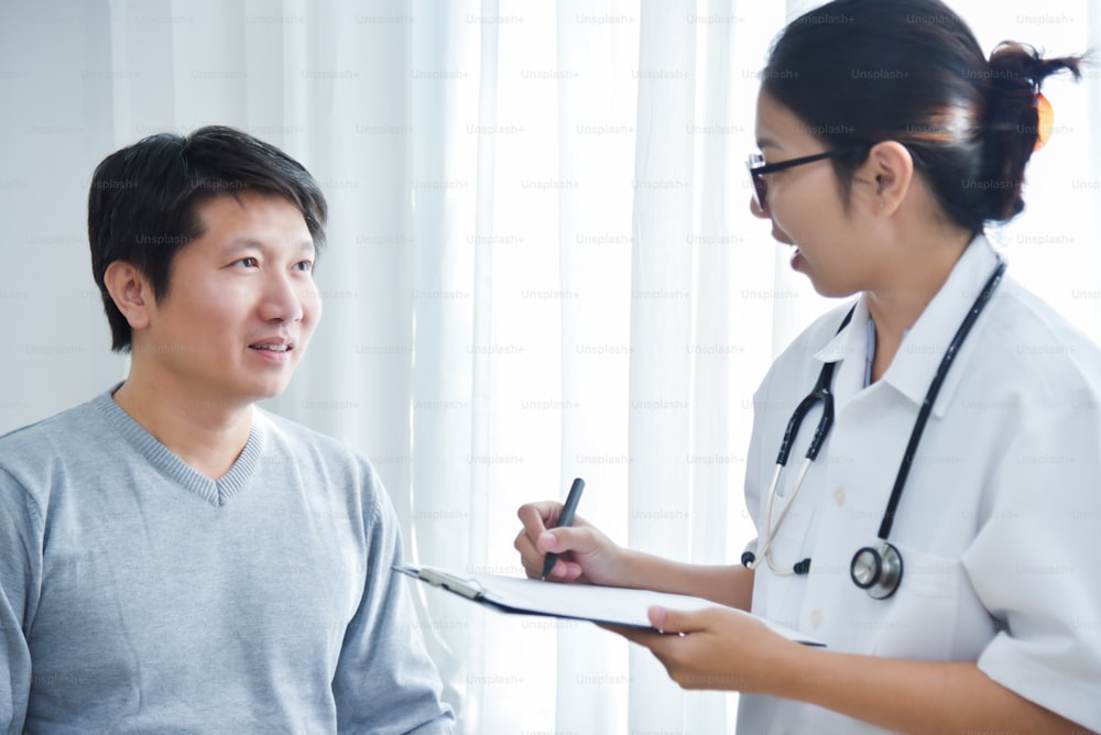 Medico asiatico che esamina e prende nota sulla carta della lista di controllo con i pazienti maschi nella stanza medica.