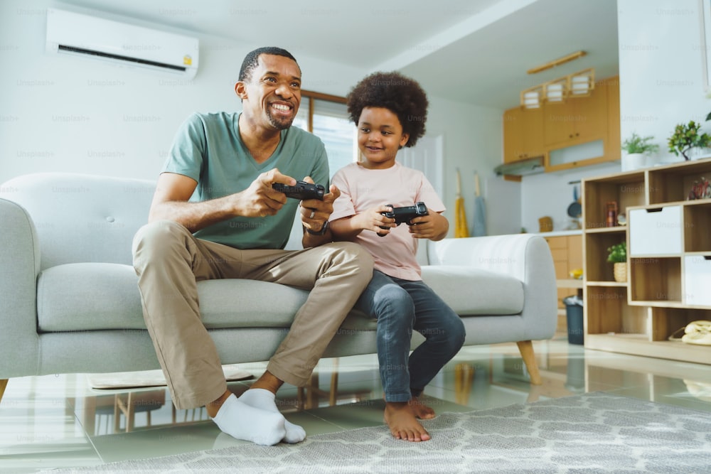 Black African American Father and his little son sitting on the couch playing video games at home