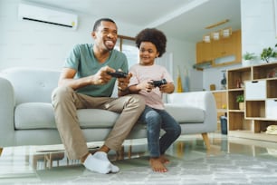 Black African American Father and his little son sitting on the couch playing video games at home