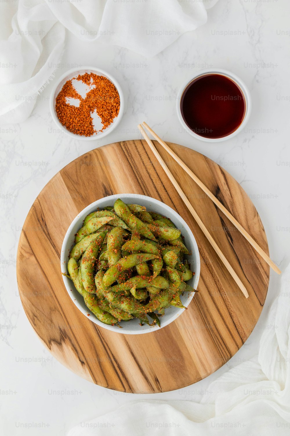 a bowl of green beans with chopsticks on a wooden board