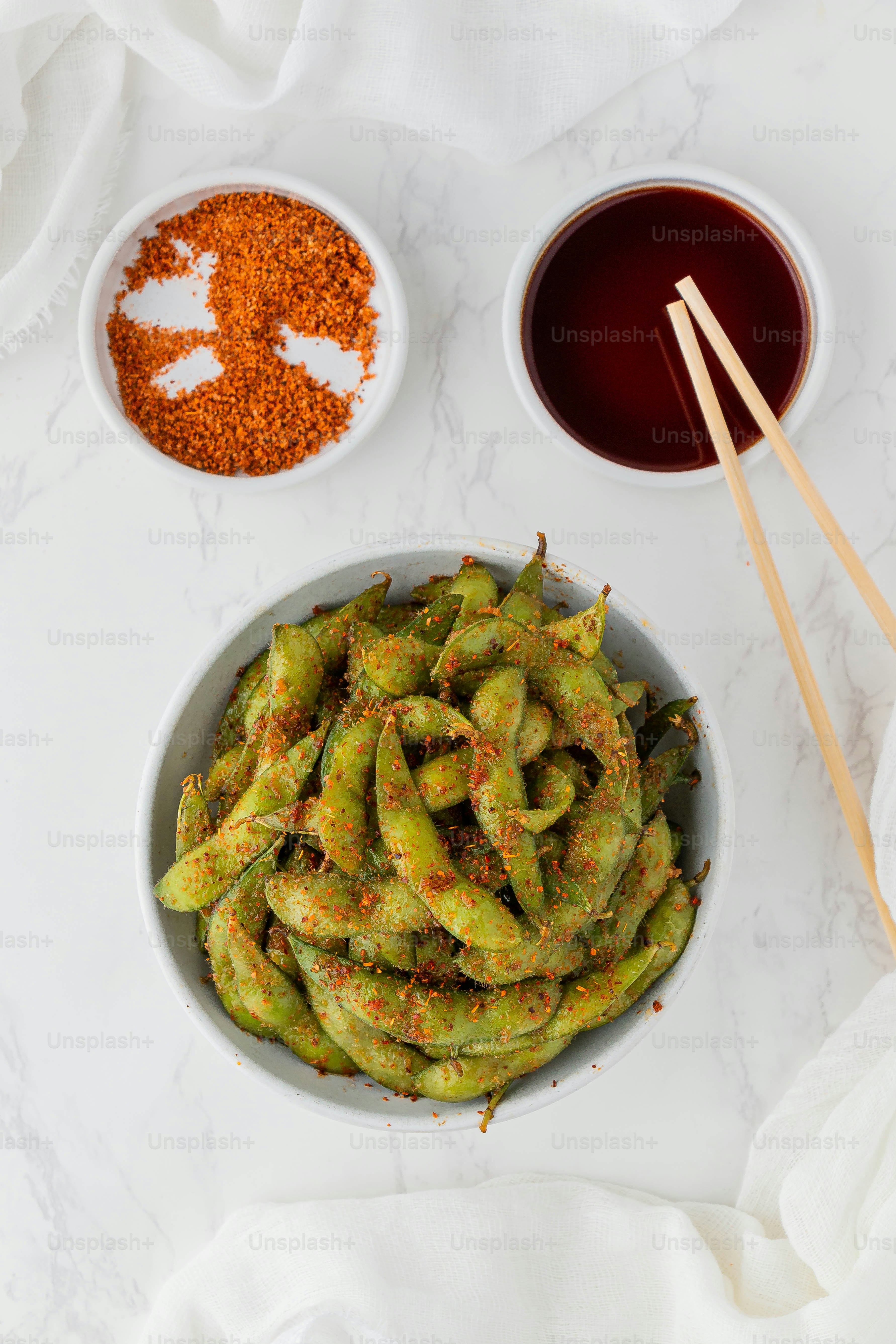a bowl filled with green beans next to two bowls of sauce