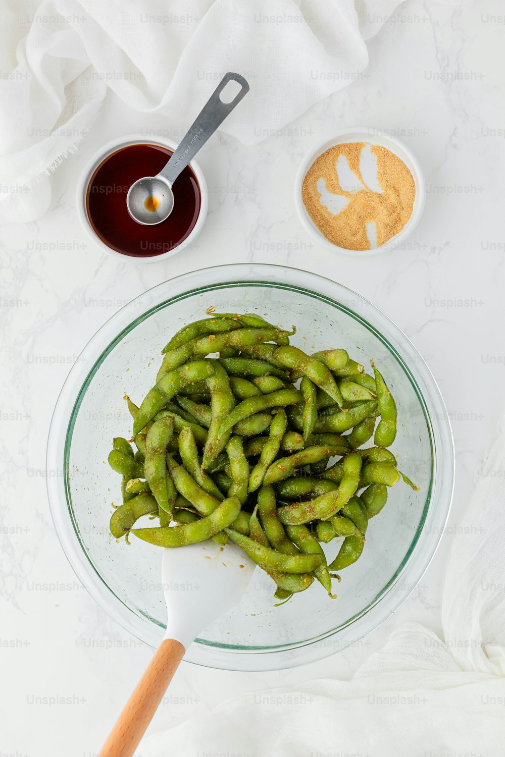 a glass bowl filled with green beans next to a spoon