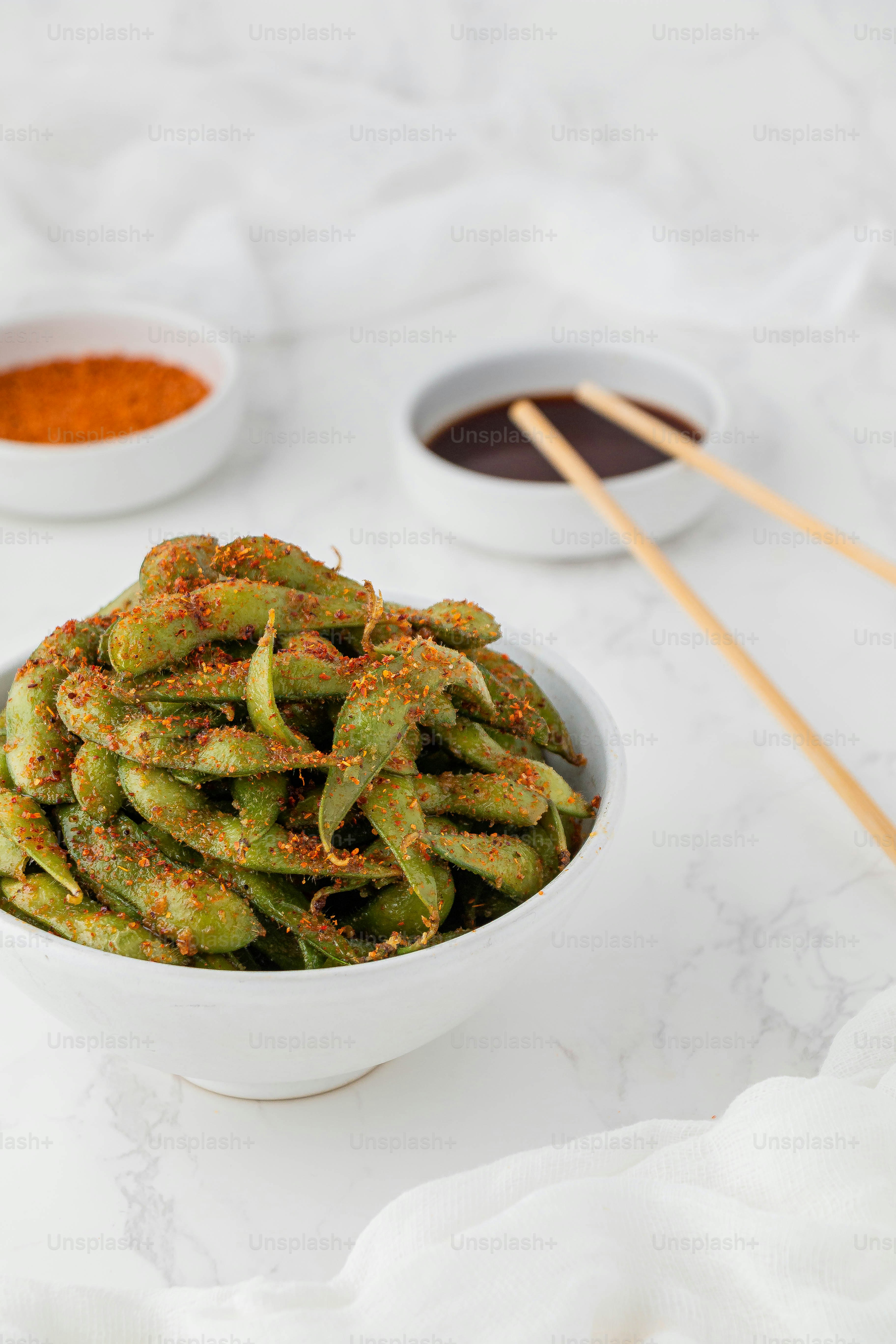 a white bowl filled with green beans next to two bowls of dipping sauce