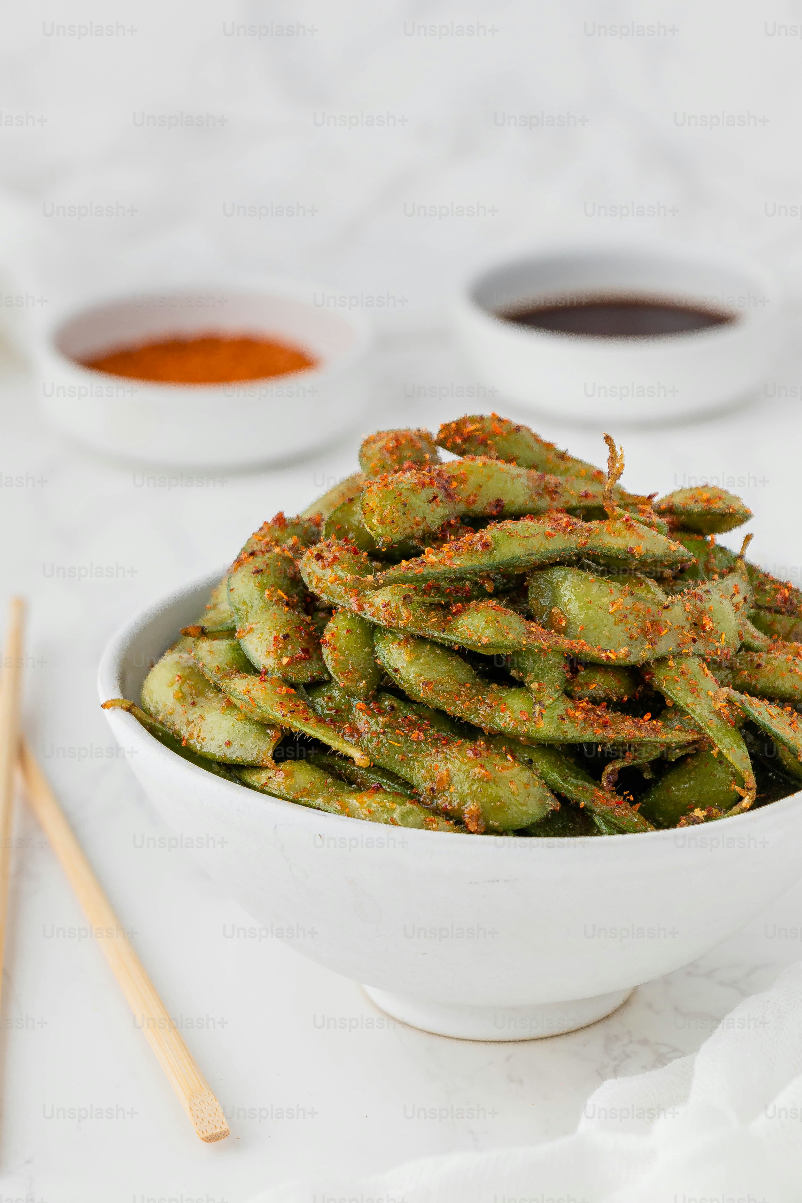 a white bowl filled with green beans next to dipping sauces