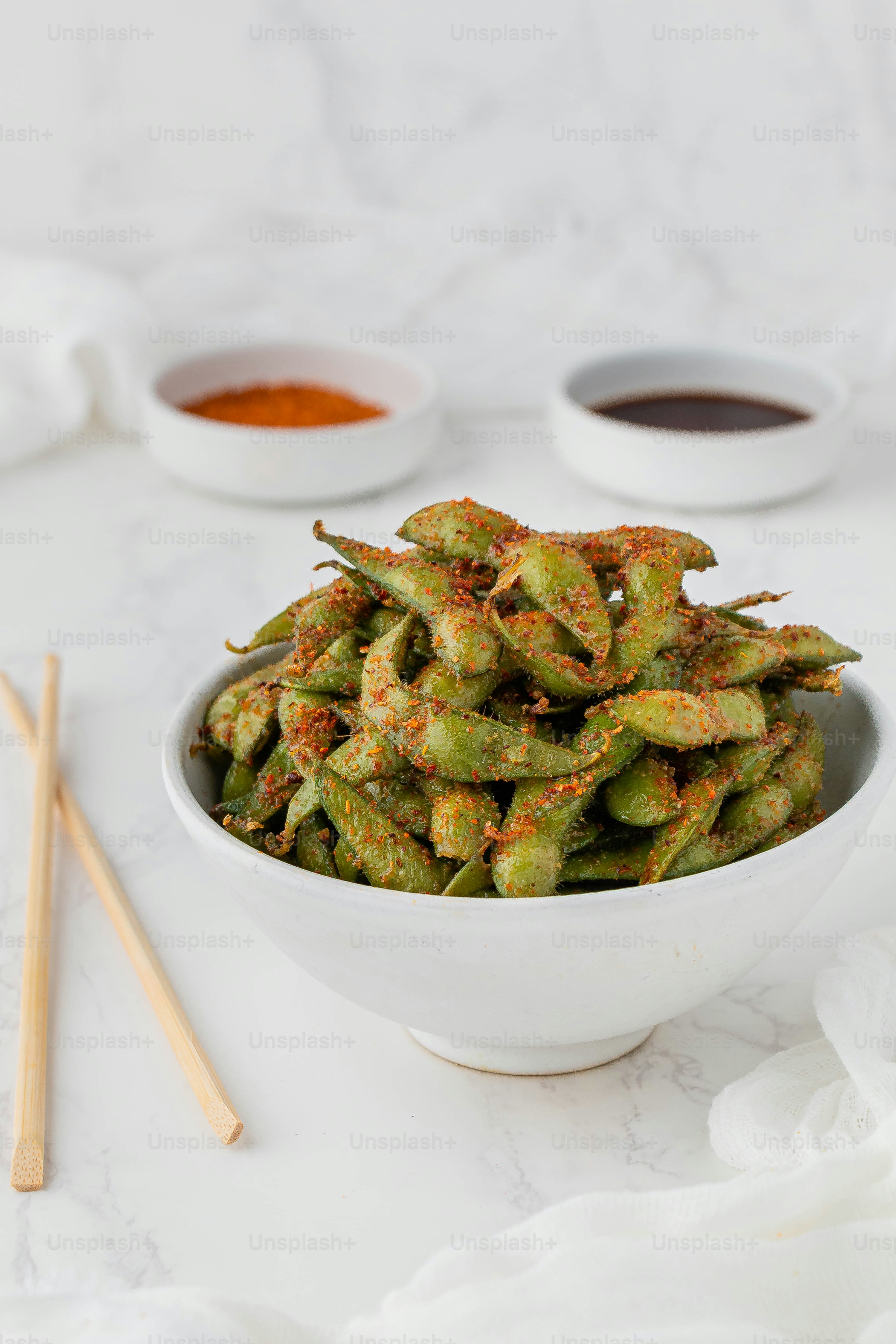 a white bowl filled with green beans next to two dipping sauces