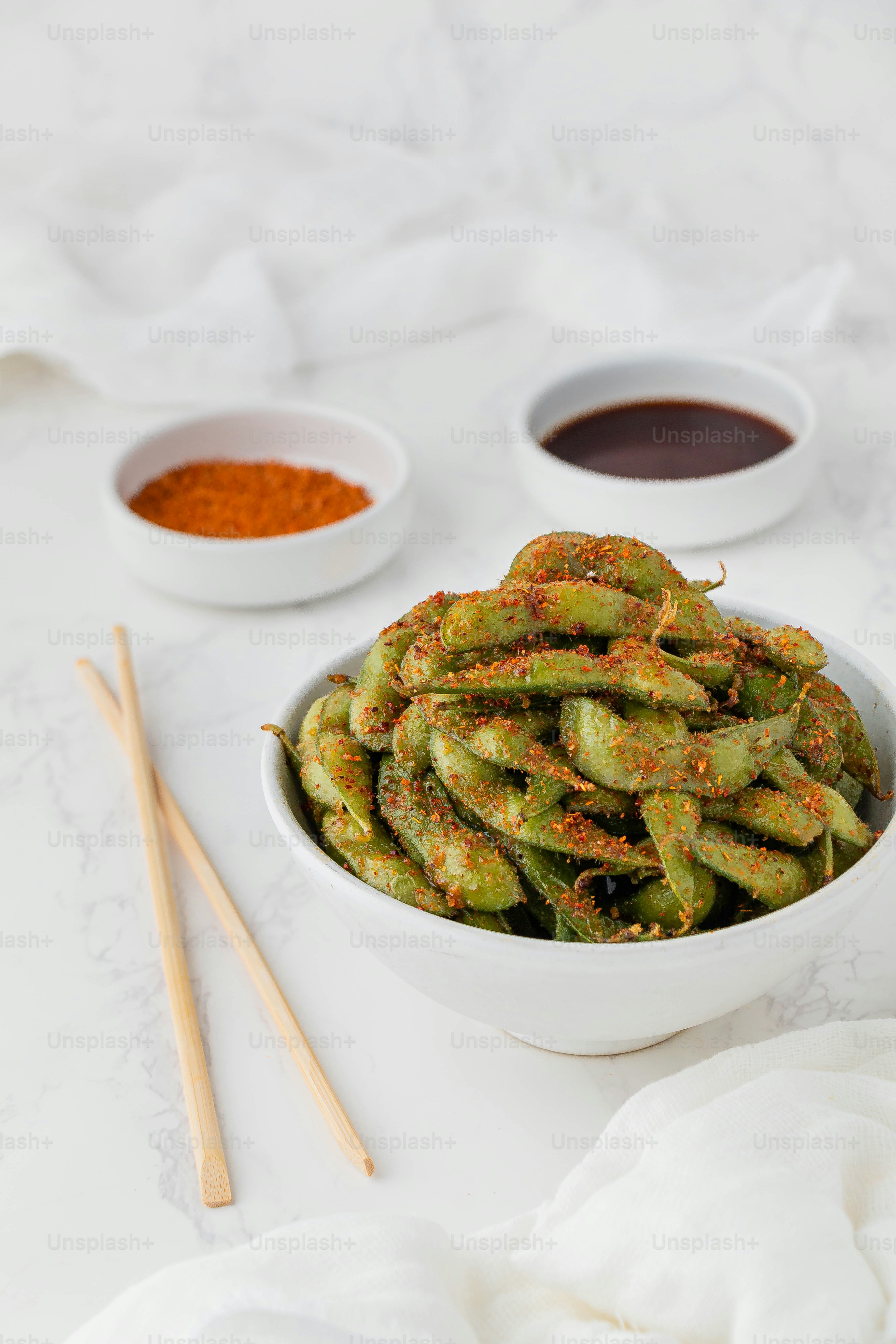 a white bowl filled with green beans next to two bowls of sauce