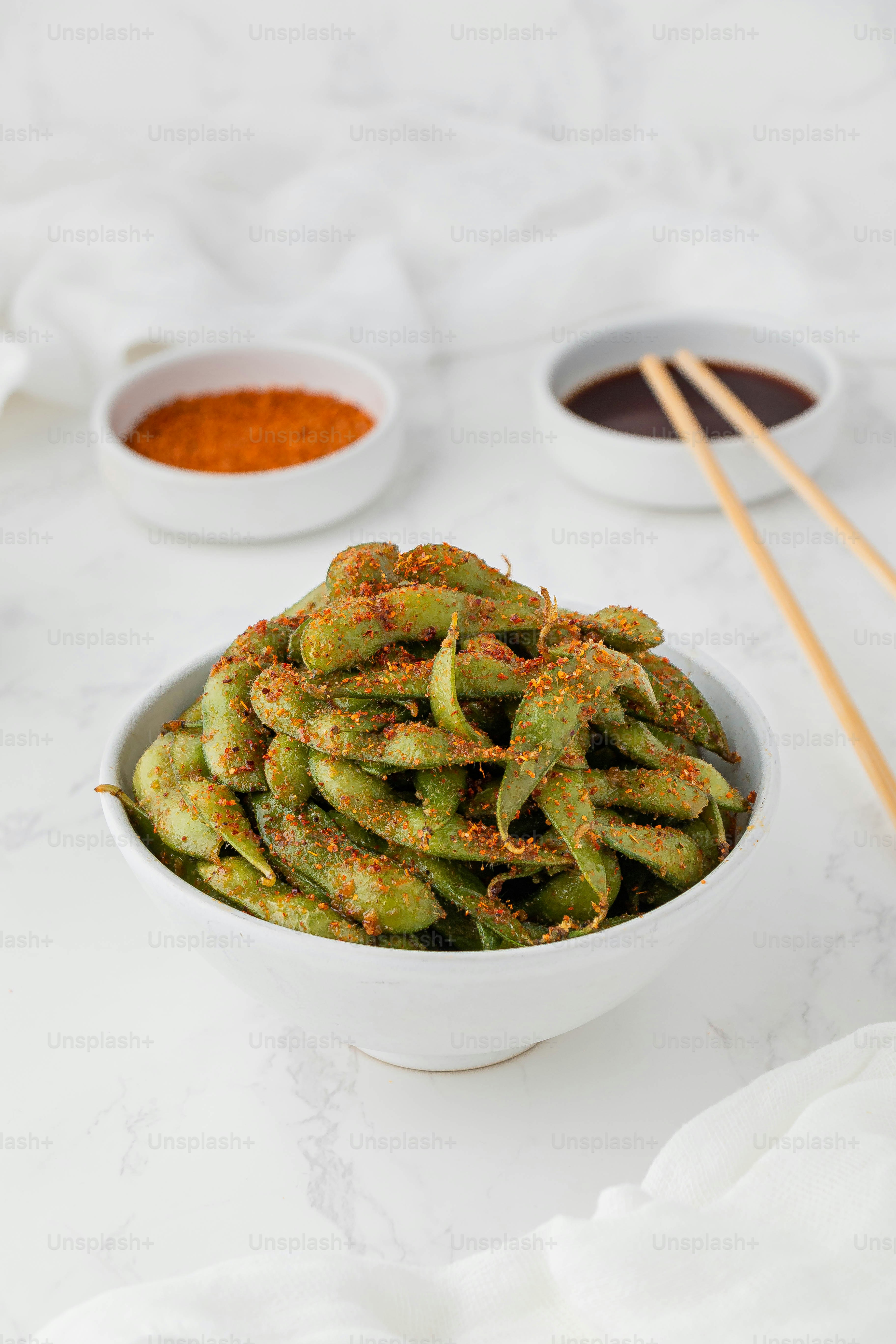 a white bowl filled with green beans next to two bowls of sauce