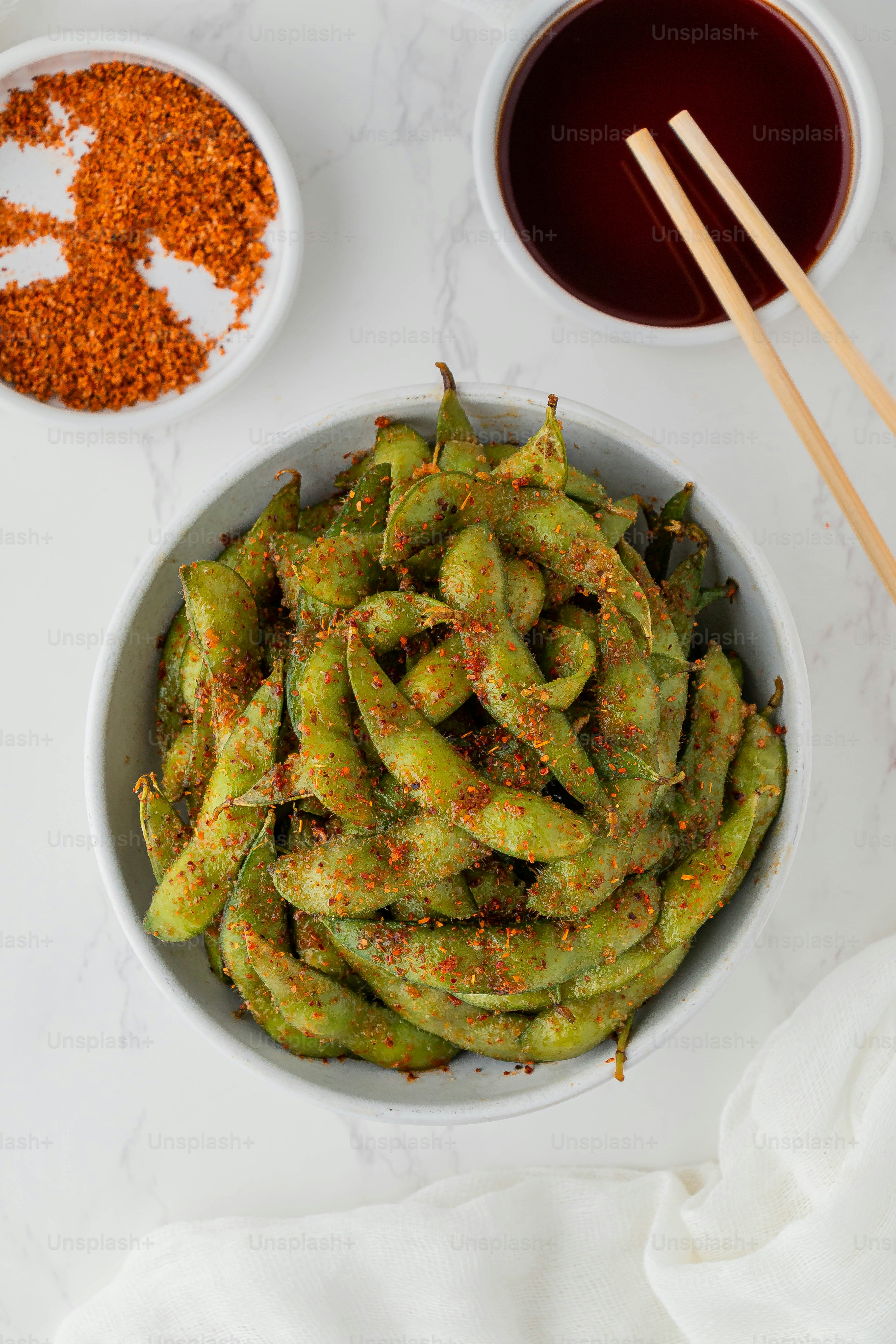 a white bowl filled with green beans next to two bowls of seasoning