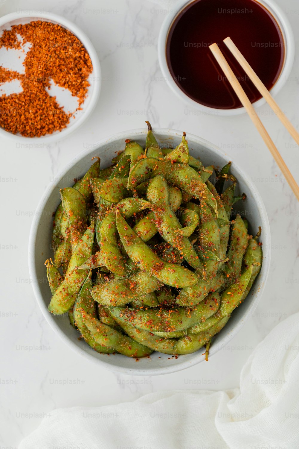 a white bowl filled with green beans next to two bowls of seasoning