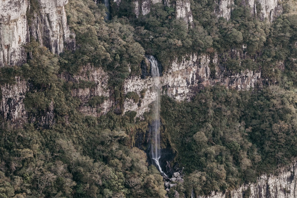 a waterfall in the middle of a mountain surrounded by trees