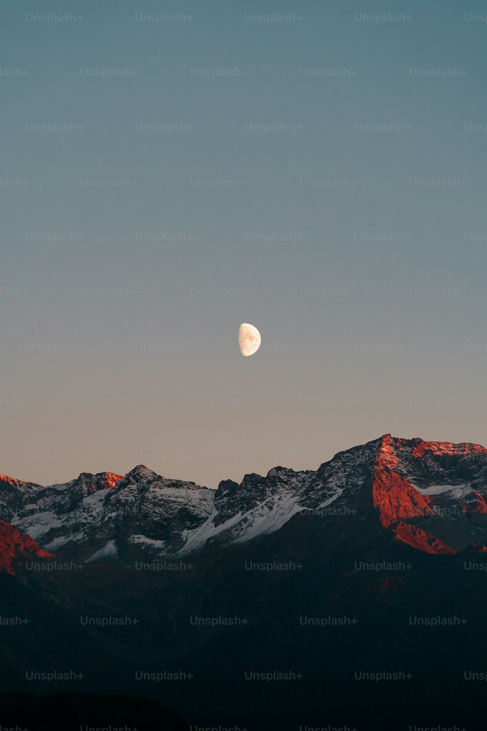 the moon is setting over a mountain range