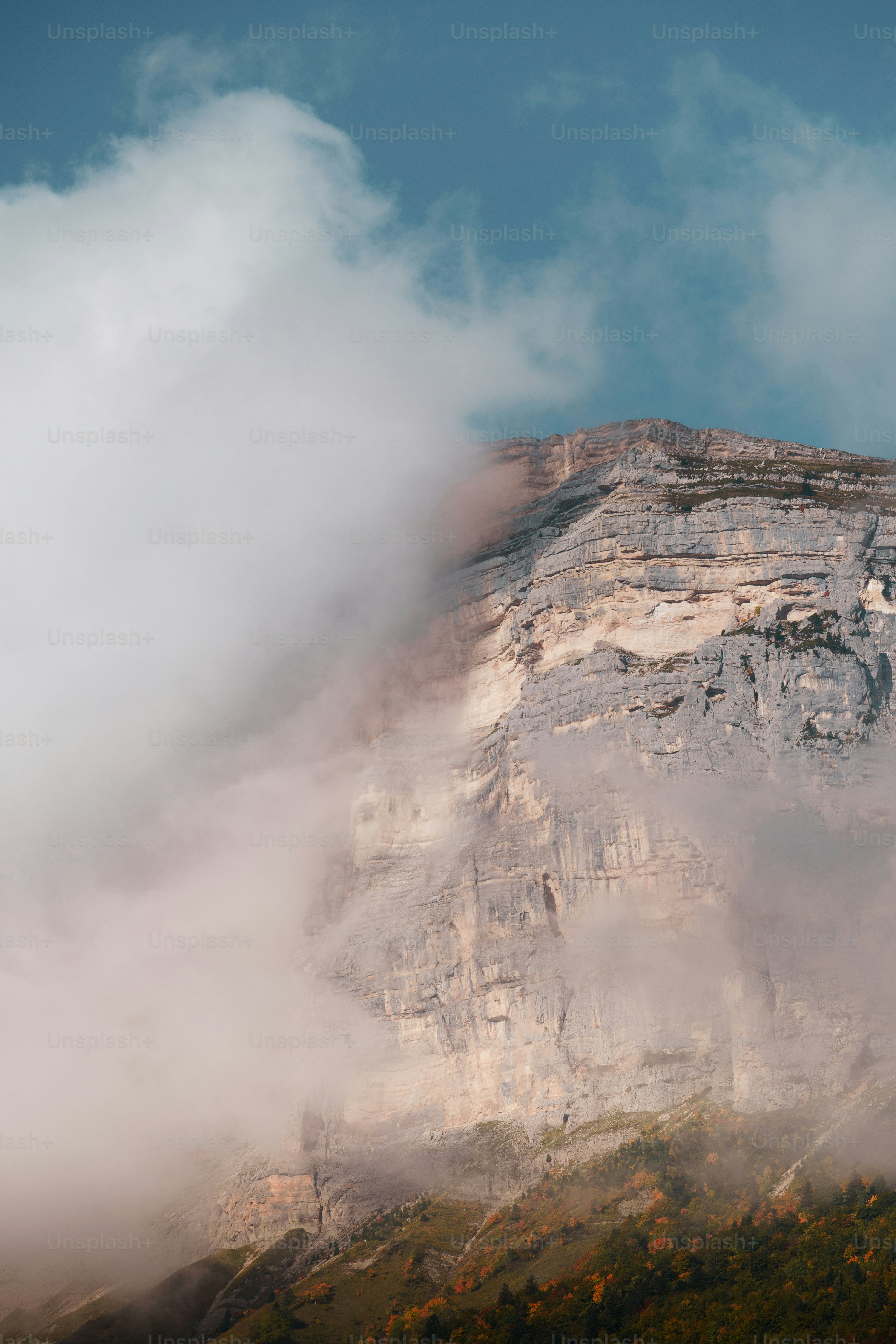 a mountain covered in fog and clouds under a blue sky