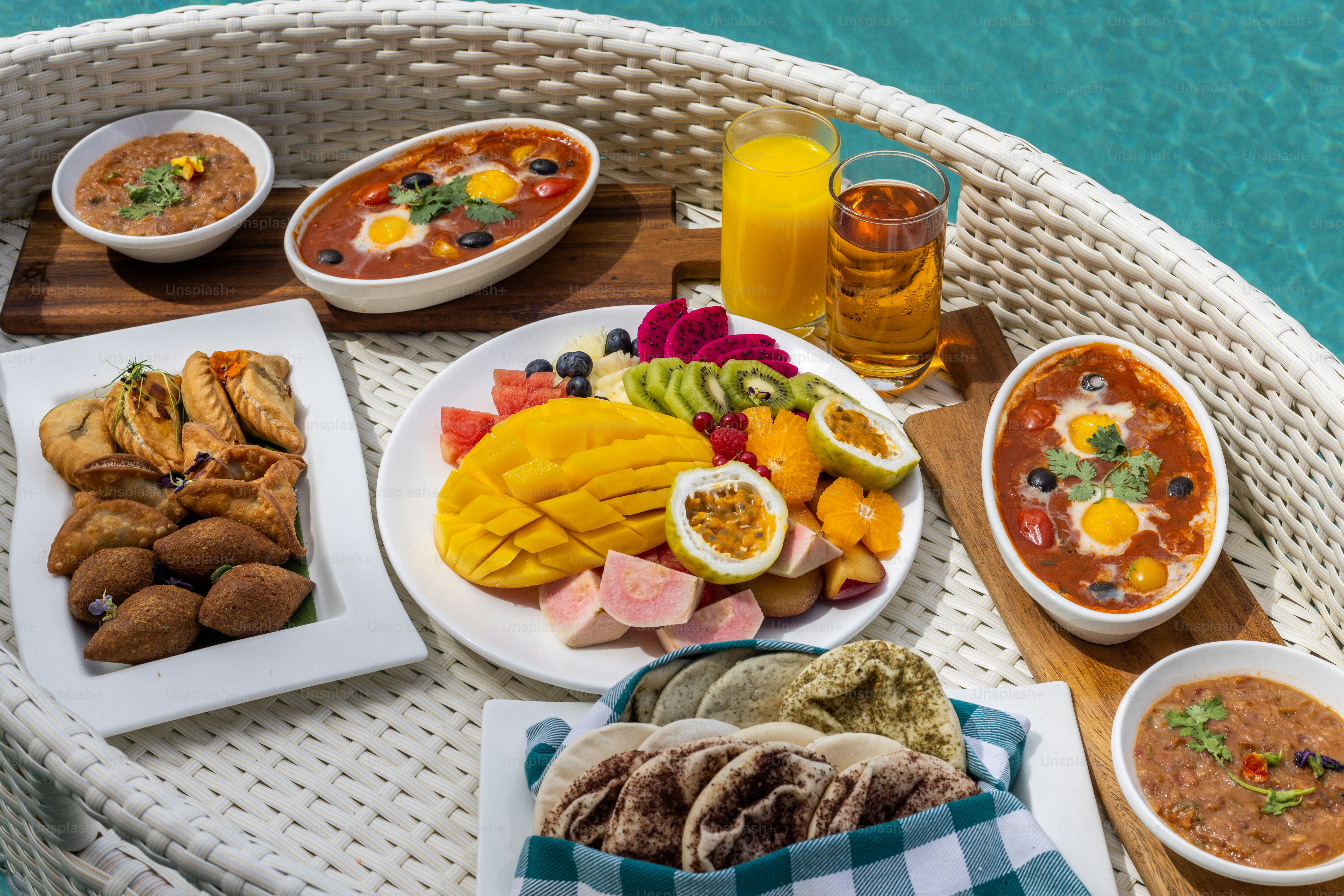 a wicker table topped with plates of food next to a pool