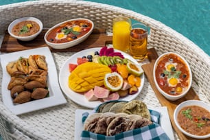 a wicker table topped with plates of food next to a pool