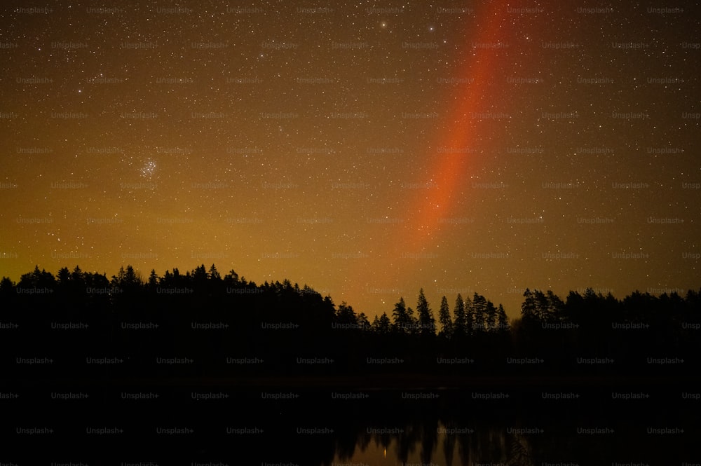 Uma luz laranja brilhante brilha no céu noturno sobre um lago