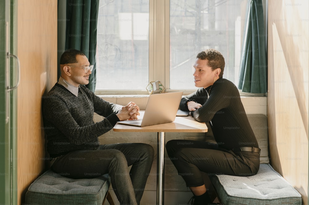 two men sitting at a table with a laptop