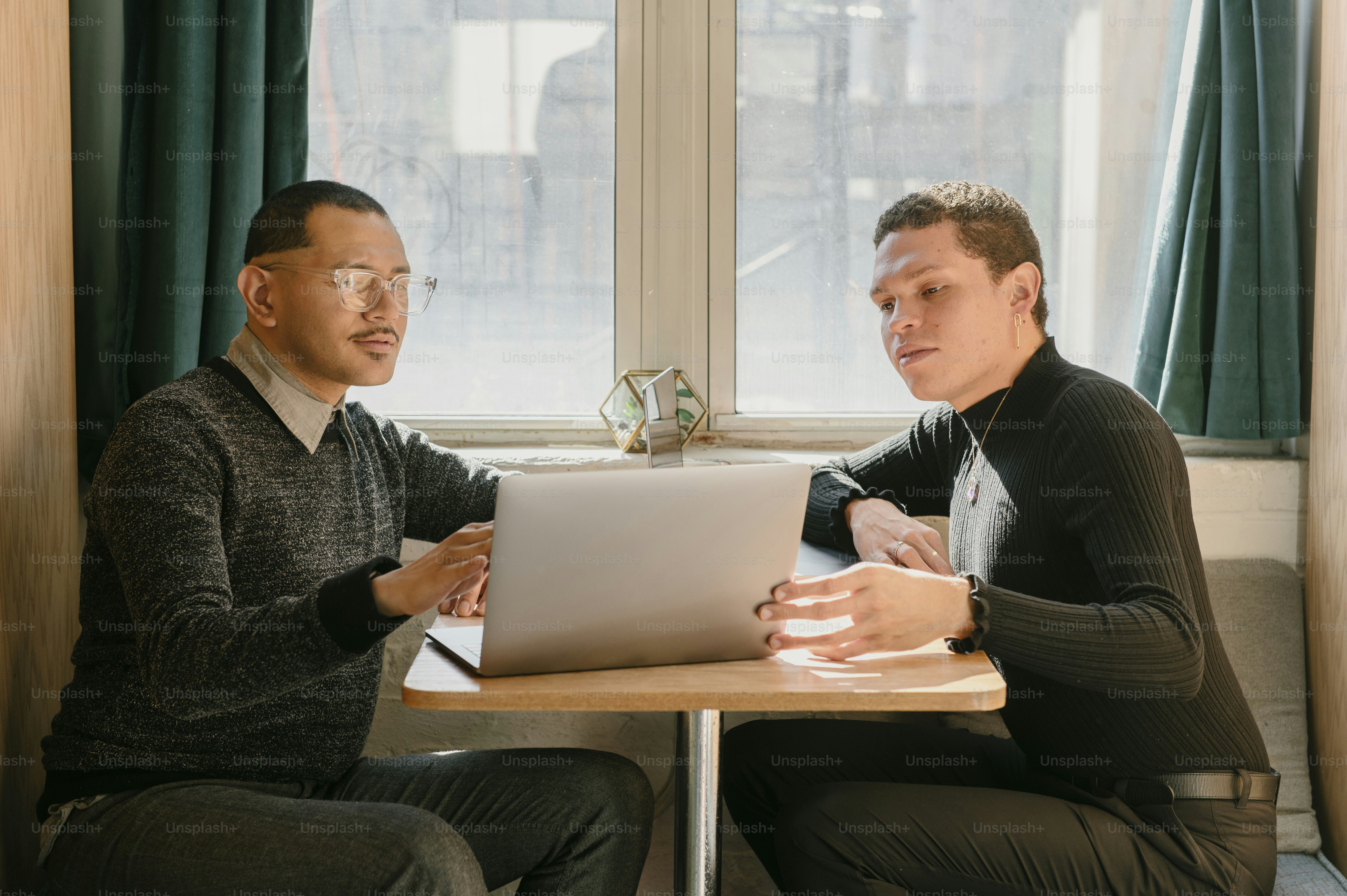 Dos hombres sentados en una mesa mirando una computadora portátil