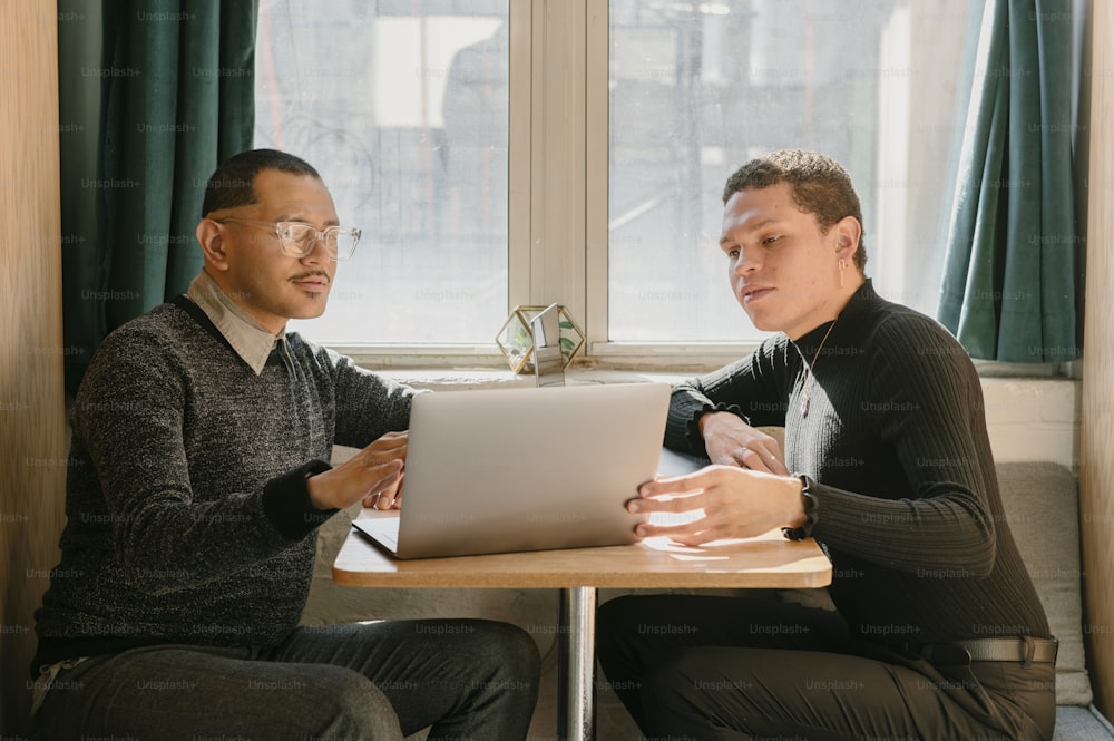 two men sitting at a table looking at a laptop