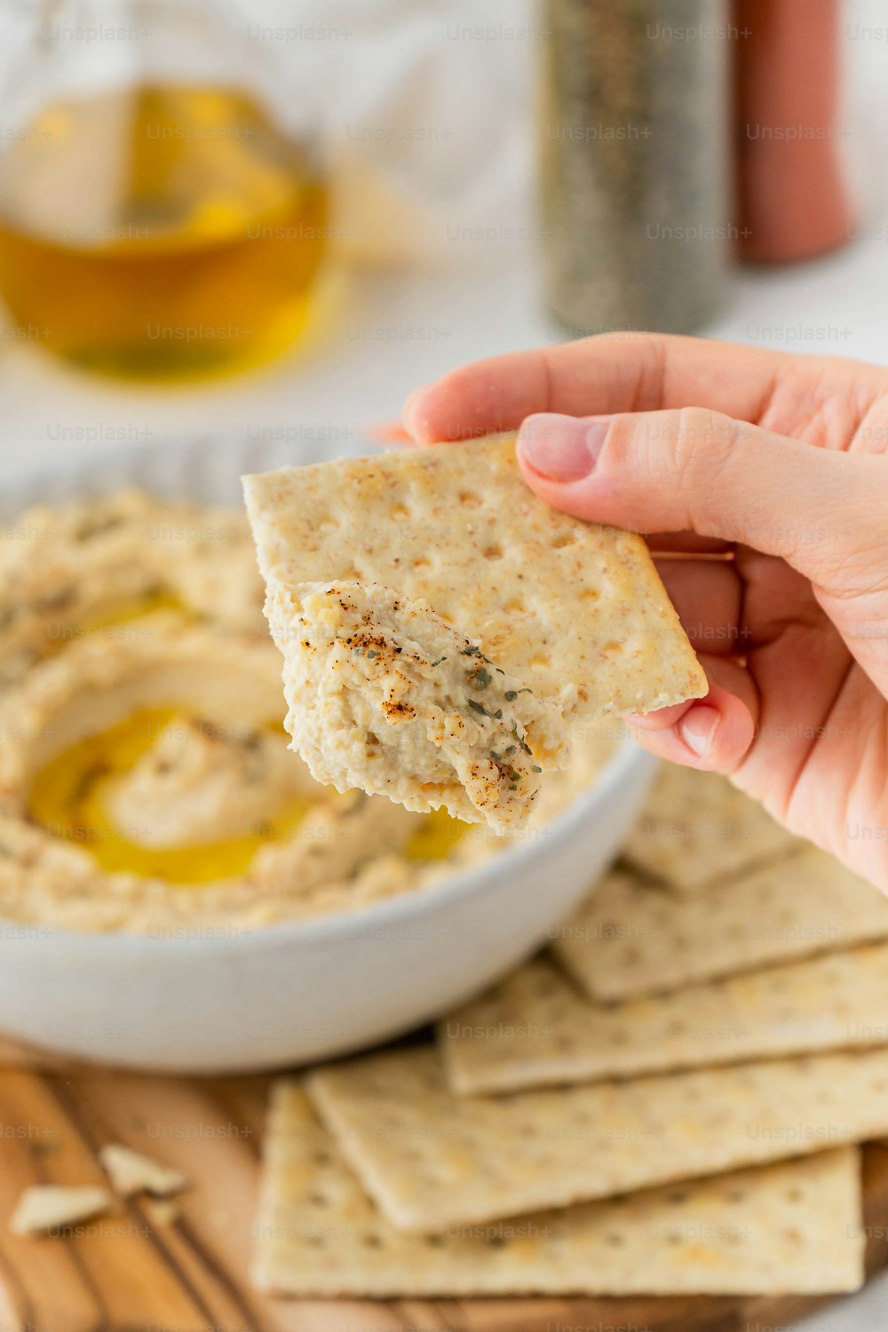 a hand holding a cracker over a bowl of hummus