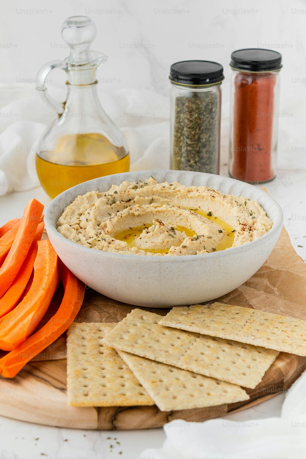 a bowl of hummus, carrots, and crackers on a cutting board