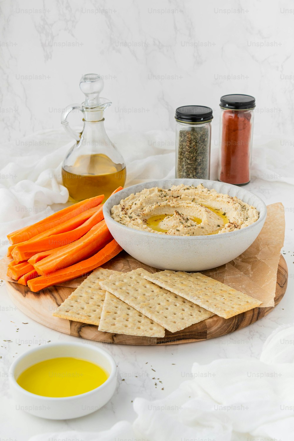 a bowl of hummus, carrots, and crackers on a board