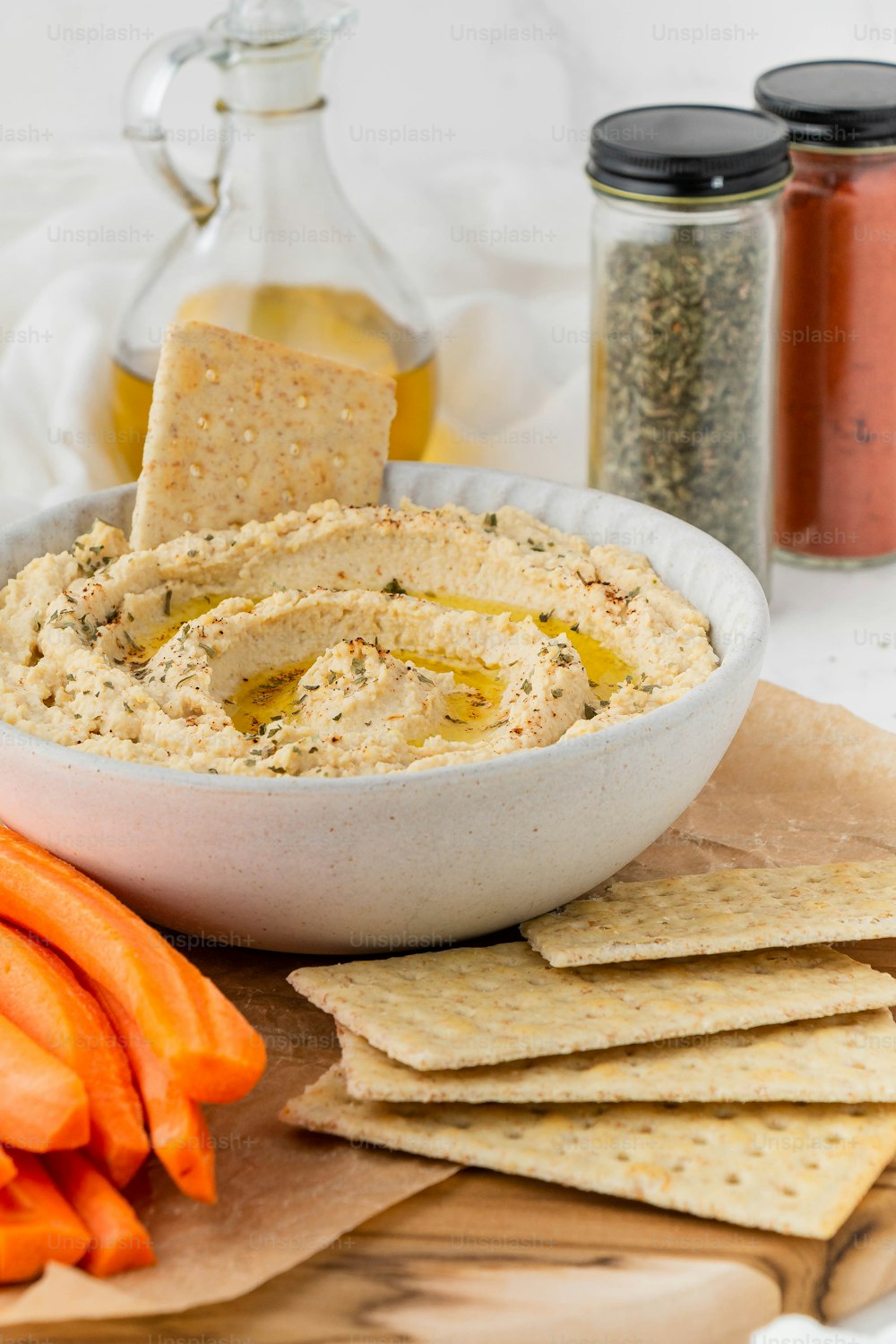 a bowl of hummus, crackers, and carrots on a cutting board