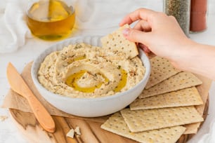 a person dipping a cracker into a bowl of hummus