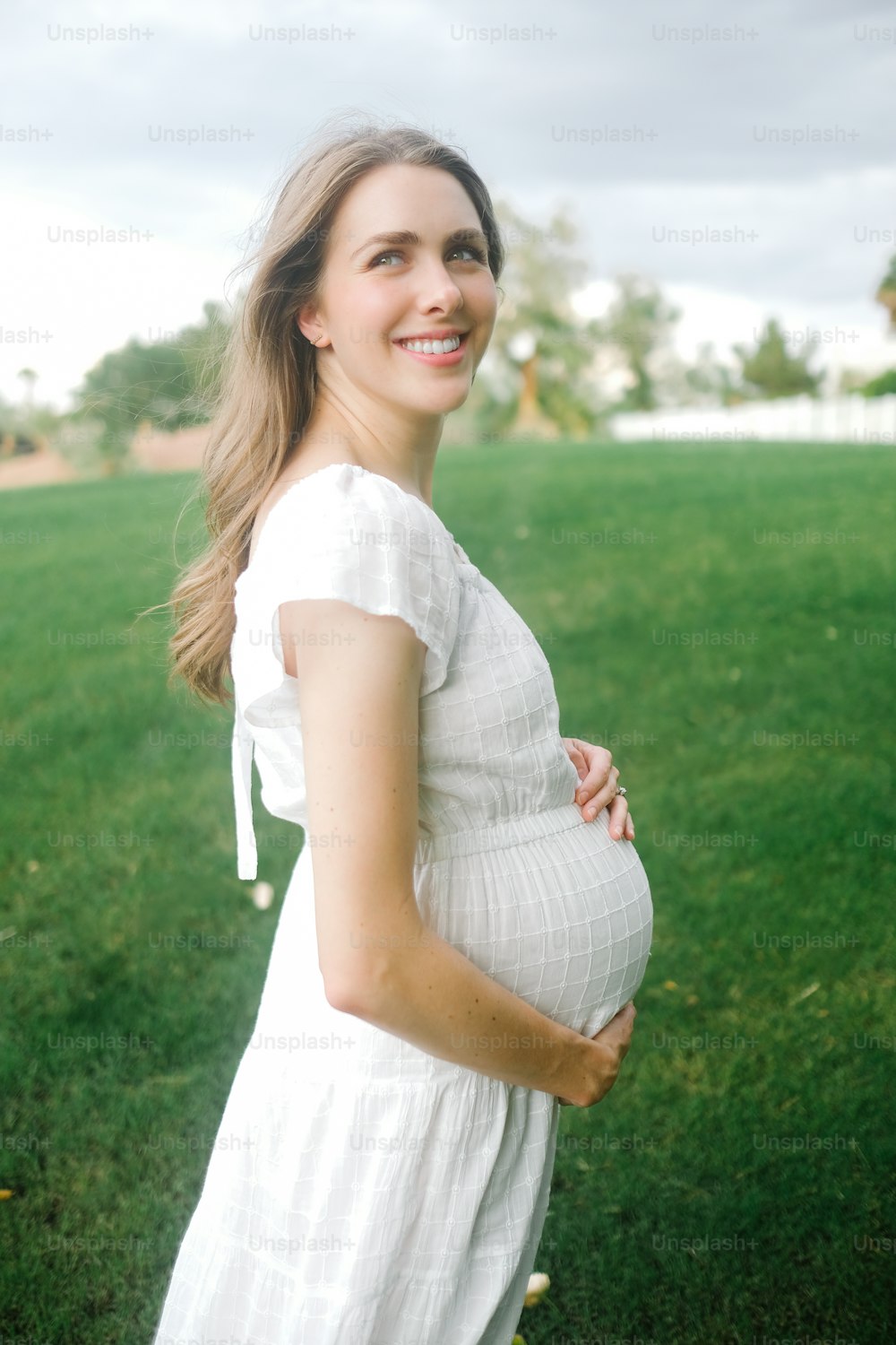 Eine schwangere Frau in einem weißen Kleid posiert für ein Foto