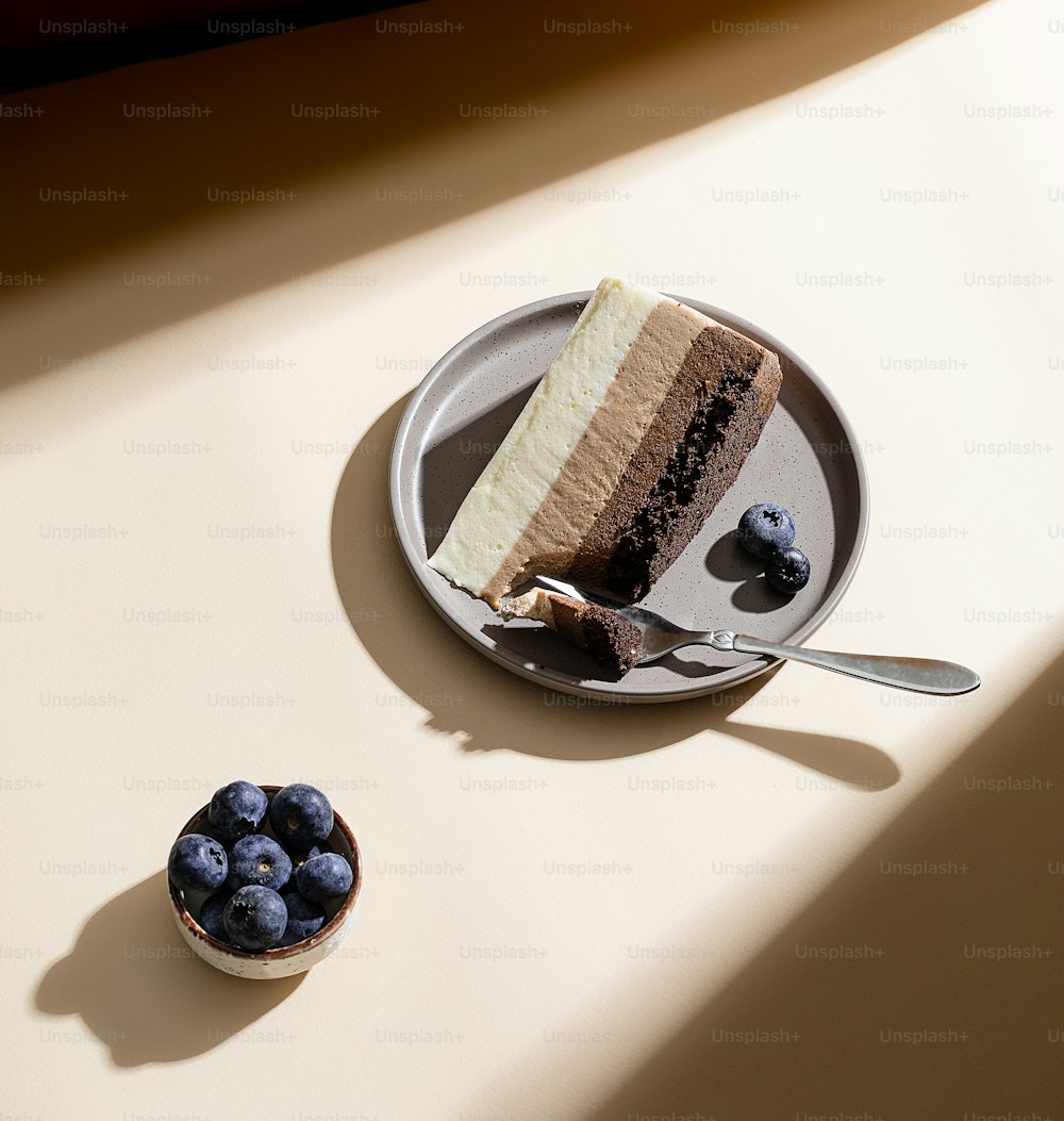 um pedaço de bolo em um prato ao lado de uma tigela de mirtilos