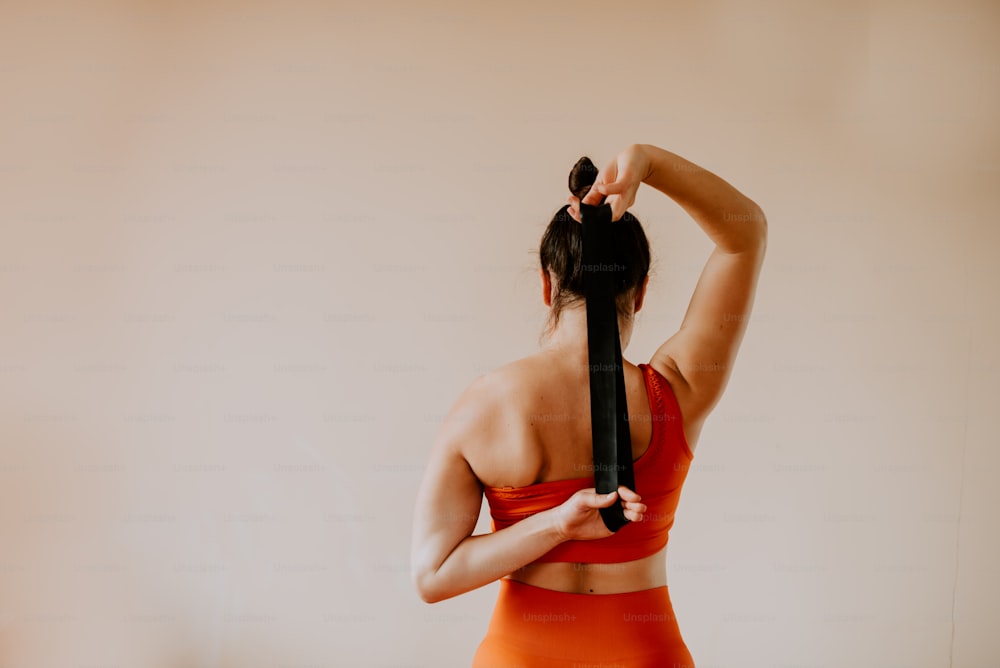 Una mujer con un sostén deportivo naranja sosteniendo un peine de cabello negro