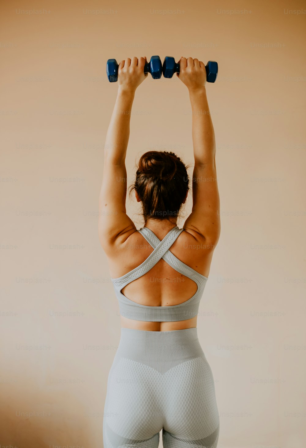 a woman in a sports bra top lifting a pair of dumbbells