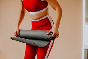 Una donna in un reggiseno sportivo rosso che tiene un tappetino da yoga